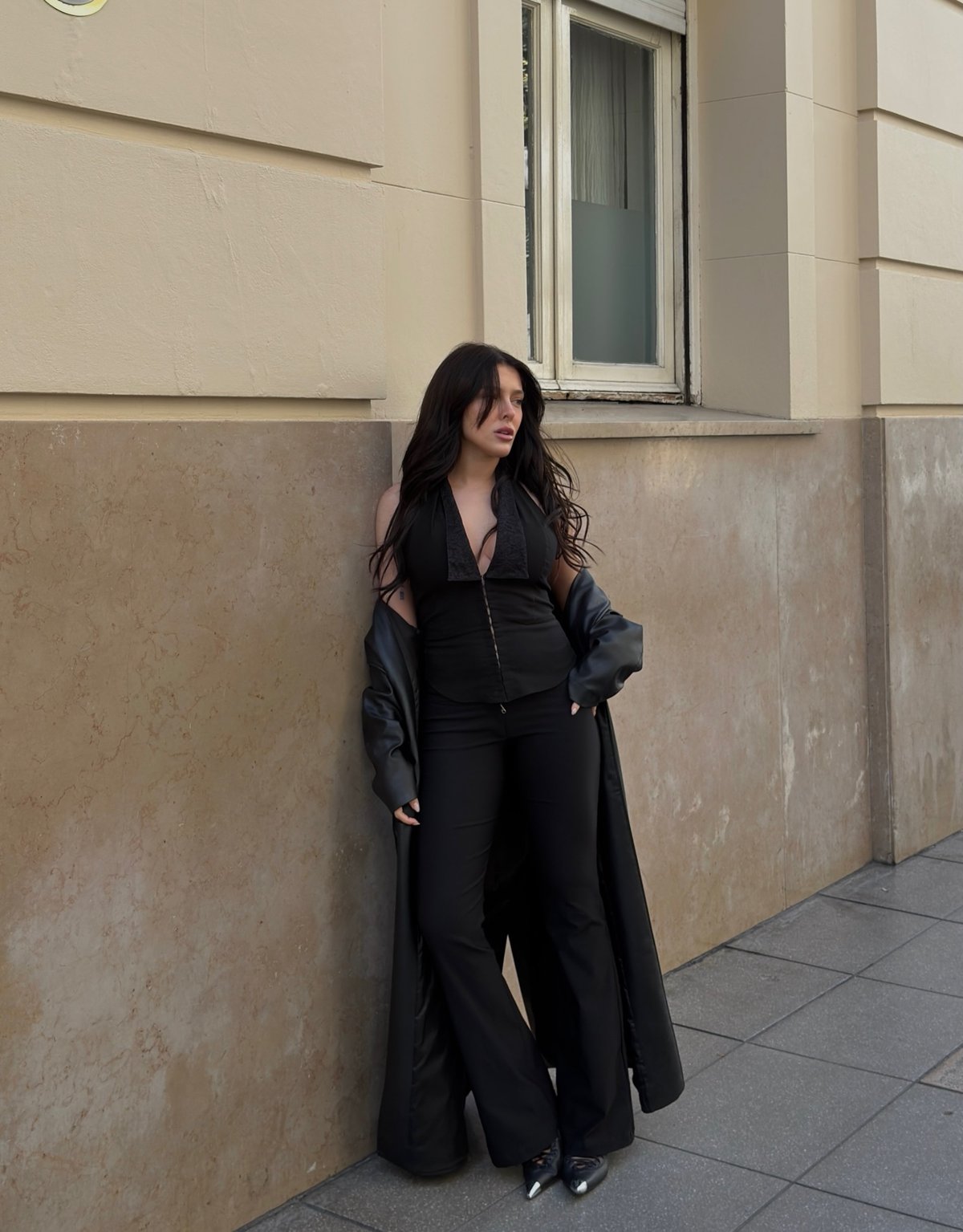 Model in a black halter and long leather coat against a stone wall