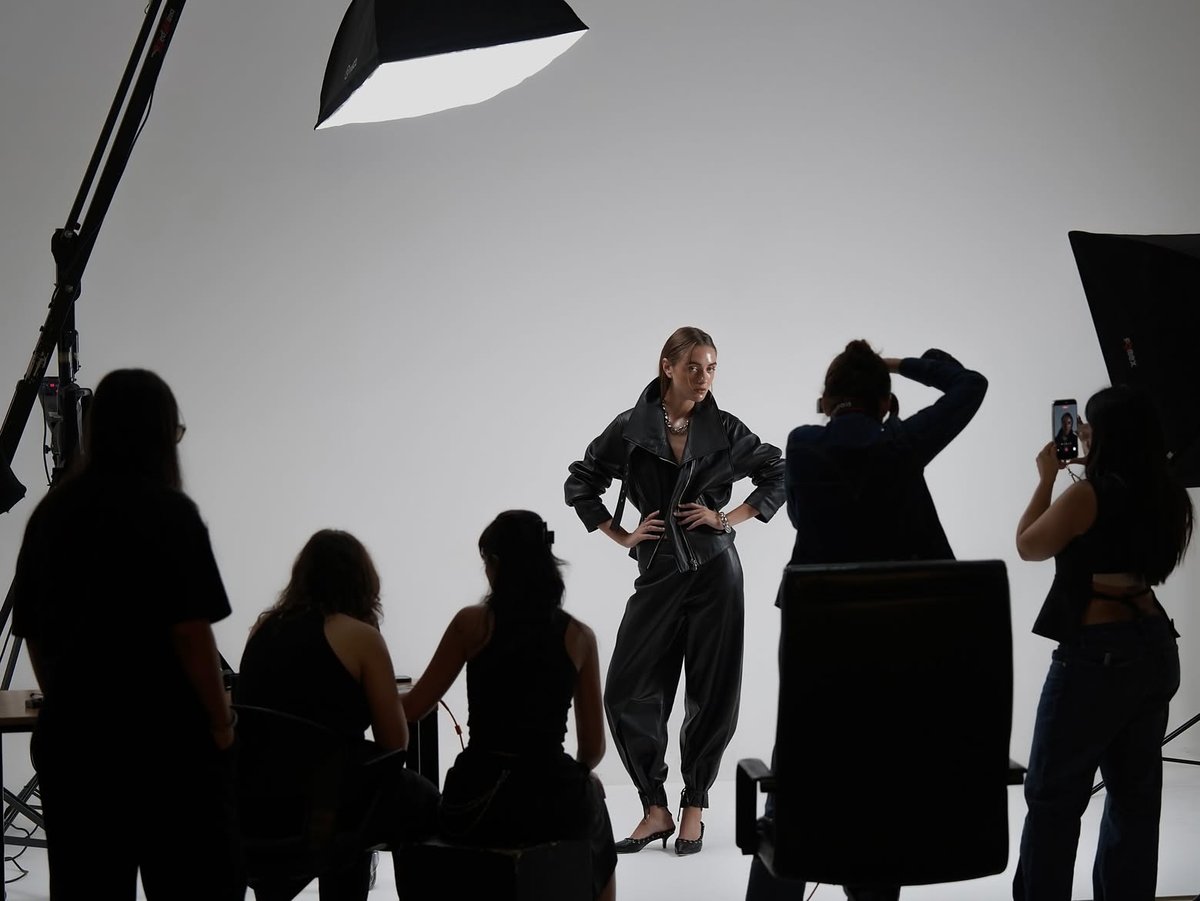 Backstage silhouettes around a model in black leather in a white studio