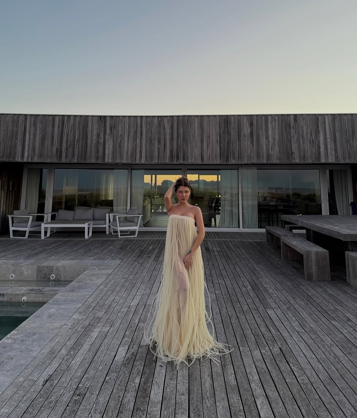 Model in a fringed ivory gown on a timber deck at dusk
