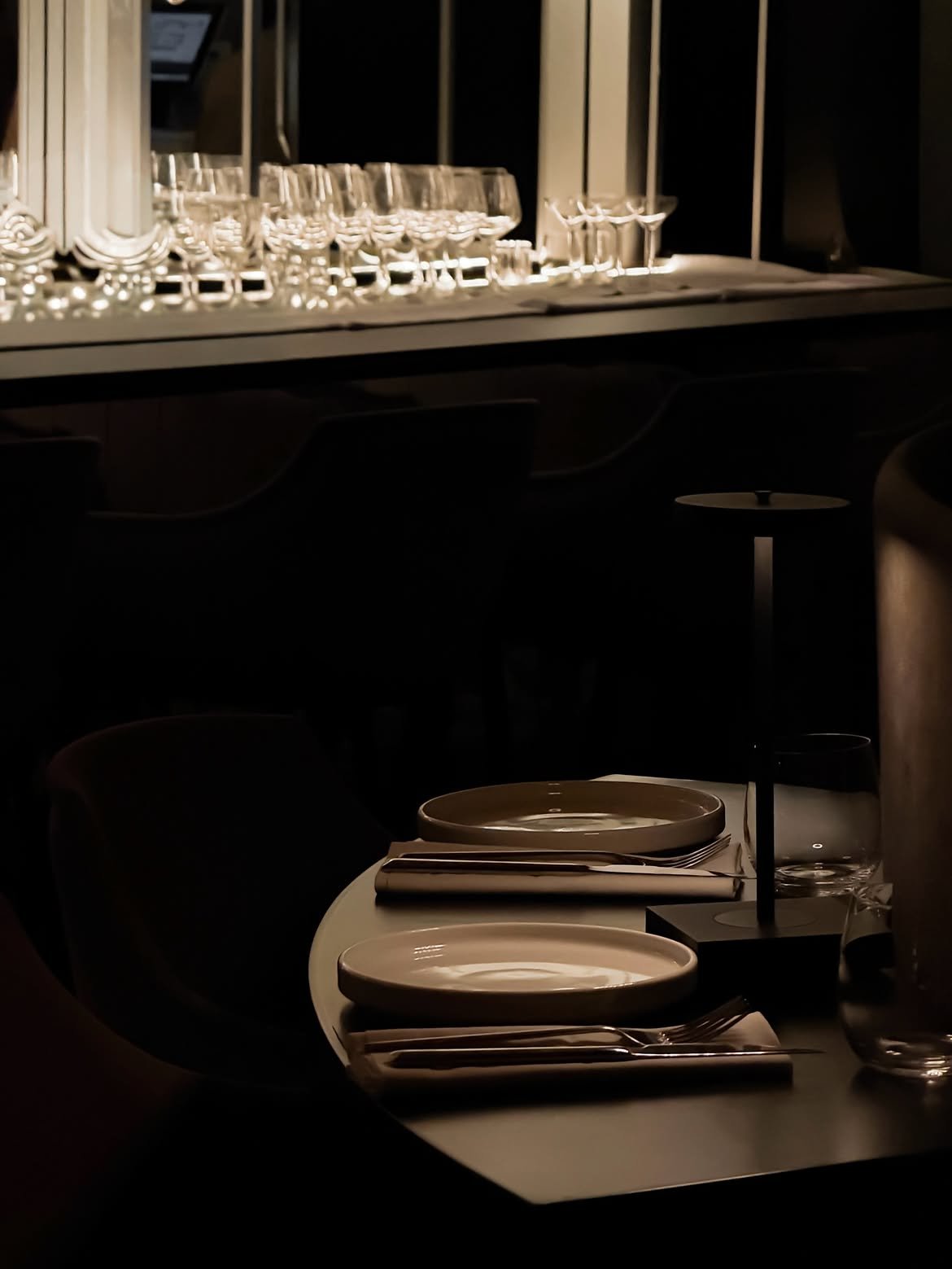 Restaurant table set in low light before a lit glass shelf