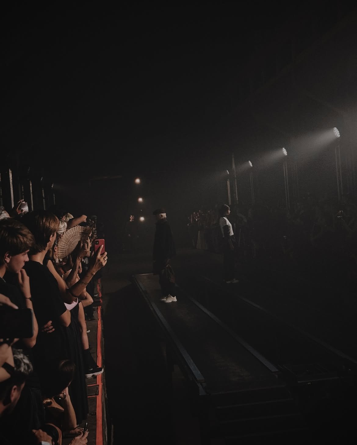 Runway show in haze, audience filming along the catwalk