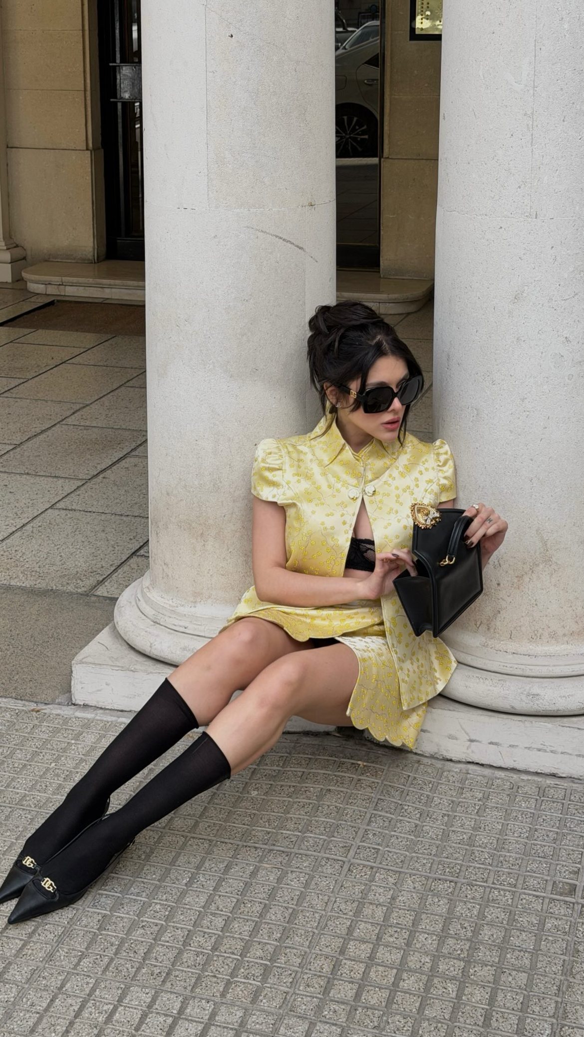 Model in a yellow floral jacquard set, knee socks and D&G slingbacks seated between stone columns