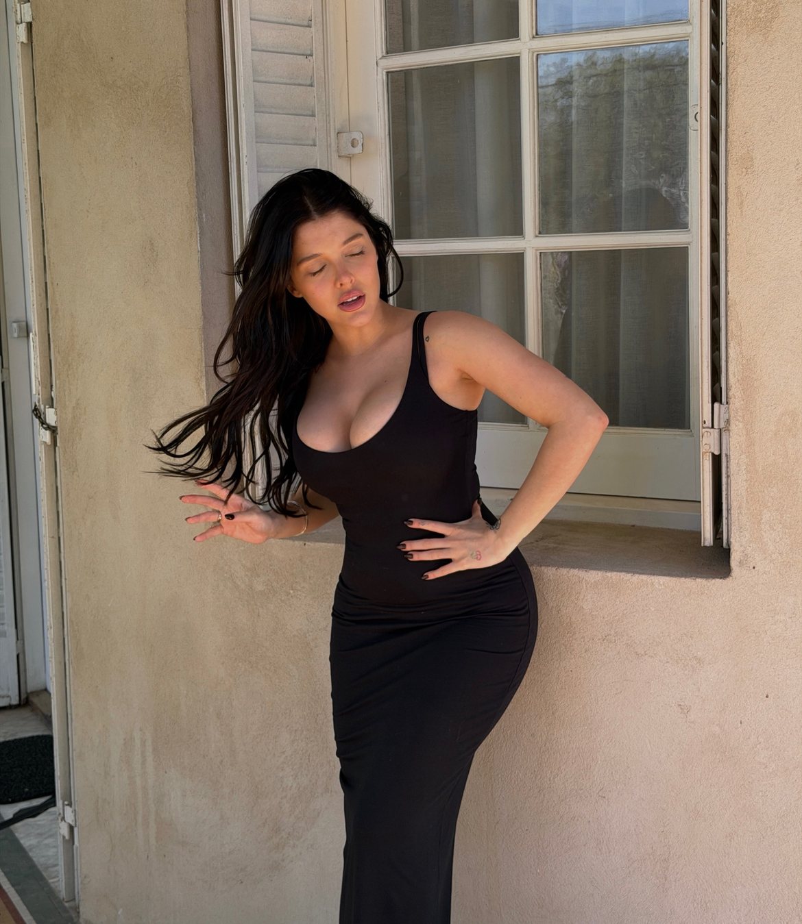Model in a black tank dress with hair in motion against a sunlit window and shutters