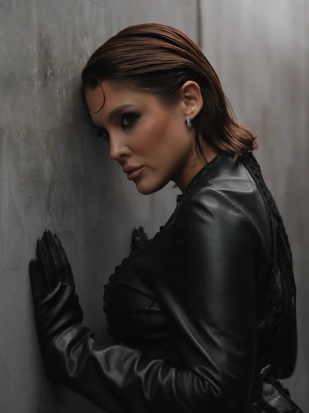 Profile of Sofía Gonet pressed to a concrete wall, slicked-back hair