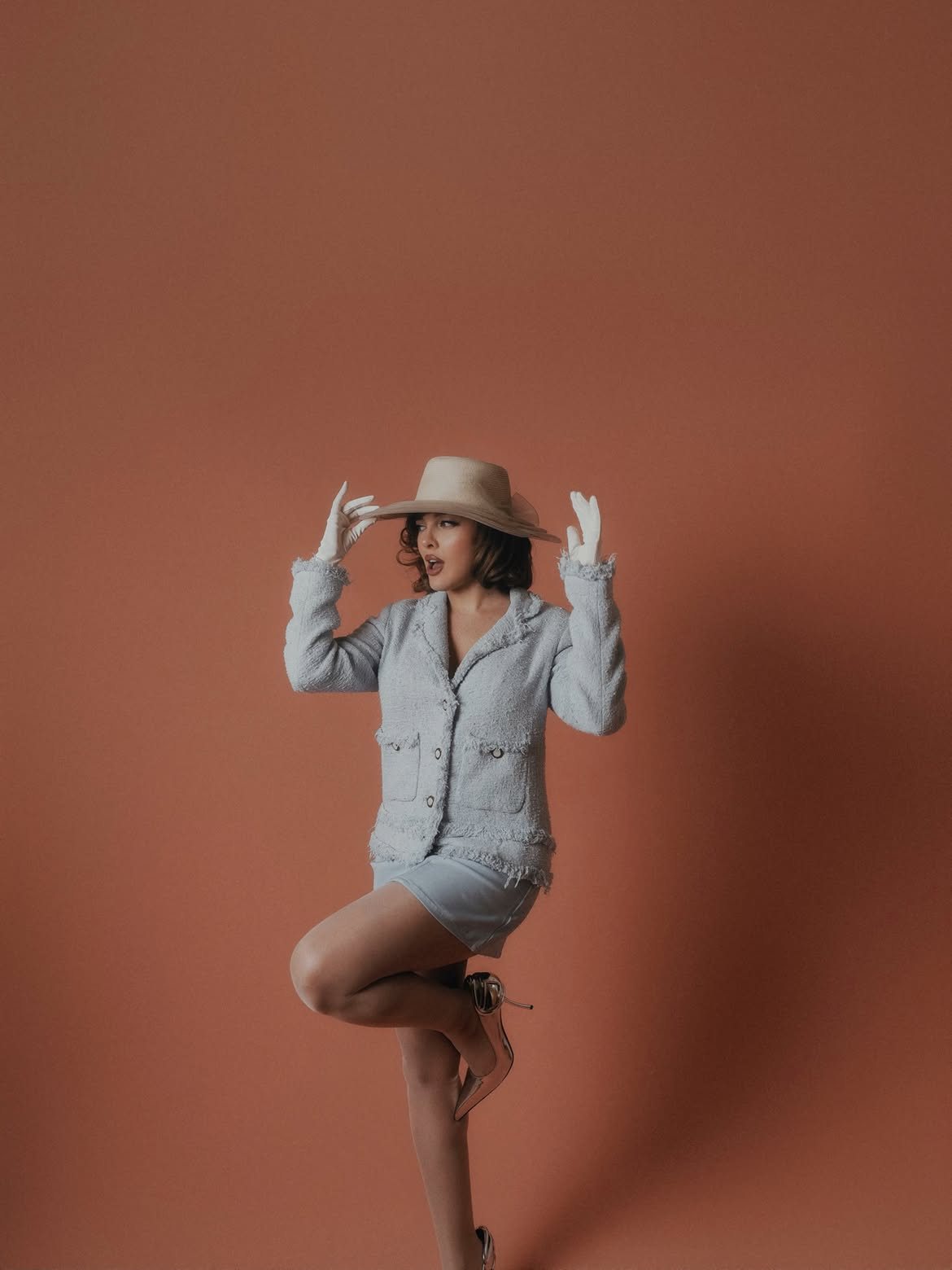 Sofía Gonet in a tweed jacket and wide hat, one leg raised against a terracotta wall